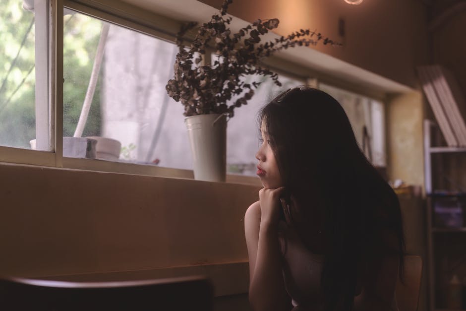 柔らかな室内照明と装飾に囲まれた窓の外を、女性が考えながら見つめています。