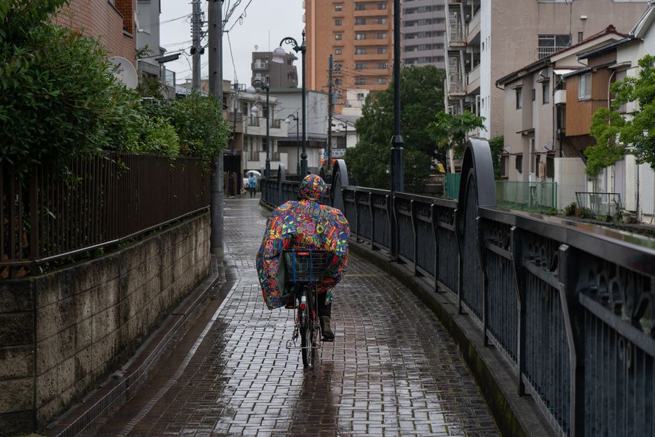 色鮮やかなレインコートを着た自転車乗りが、雨に濡れた東京の路地を走っている。